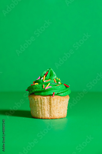 Green frosted vanilla cupcake with rainbow sprinkles on a green background