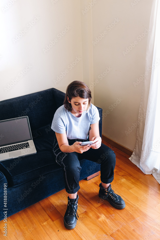 Girl typing on the cell in her living room with her winged laptop