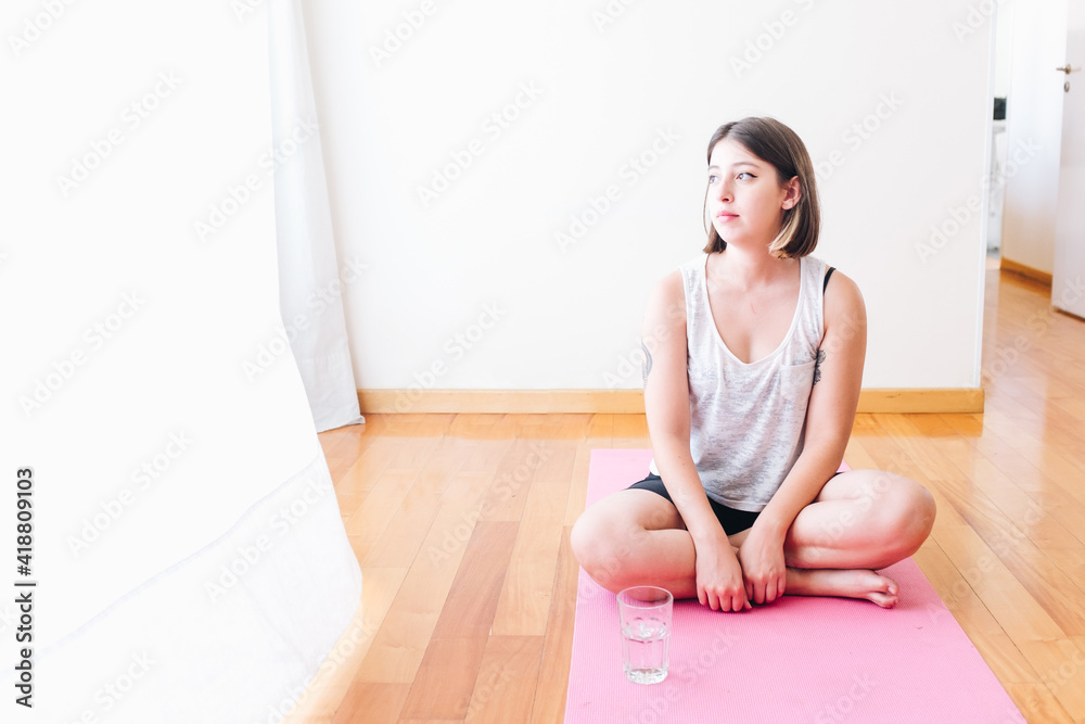 Fototapeta premium Thoughtful athlete girl sitting on the floor with a glass of water