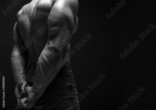Pumped up strong sweaty upper body back and biceps of brutal man athlete in jeans standing showing perfect shape over dark background. Sport men body concept photo