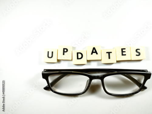 Selective focus.Glasses and scrabble letters with text UPDATES on white background.Business concept.