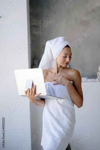 Woman freelancer in white towel stand in the bathroom with a laptop