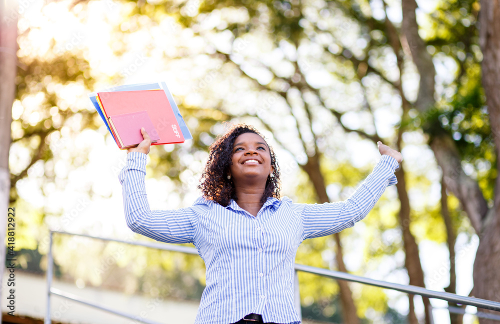 Naklejka premium Student girl celebrating and having fun. Happy girl with arms raised with trees in the background of the image.