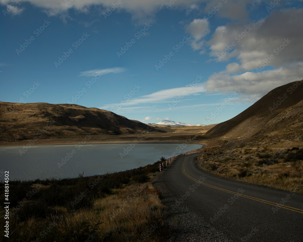 Road curving around a hill in Patagonia, with a lake on the left and a snow-capped mountain in the background.