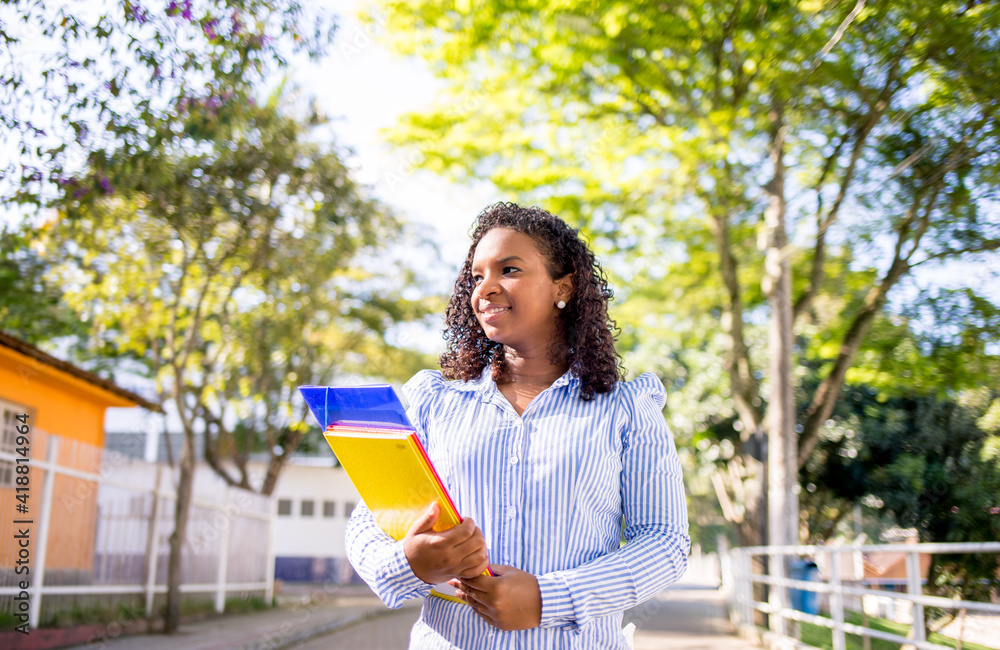 Portrait of a young college girl holding folders and notebooks and walking down the street to go to school or college. Student girl smiling and happy. Portrait of a young college girl holding folders and notebooks and walking down the street to go to school or college. Student girl smiling and happy.