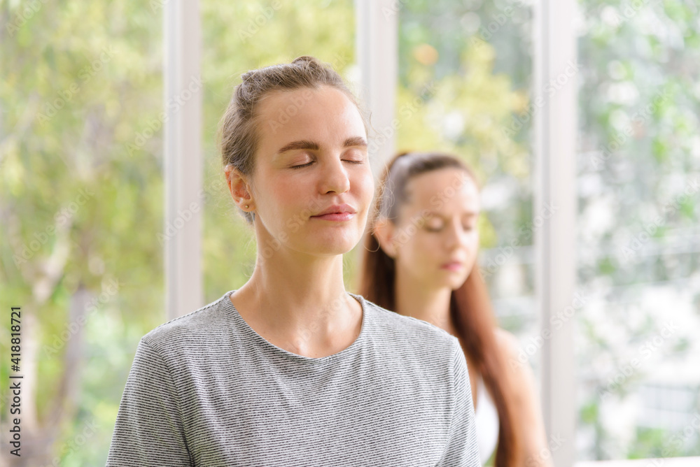 Time for practicing yoga. Two youngs attractive women sitting in Ardha Padmasana exercise, Lotus pose on meditation, closed eyes, wearing sportswear on mat at home. lifestyle concept Time for practicing yoga. Two youngs attractive women sitting in Ardha Padmasana exercise, Lotus pose on meditation, closed eyes, wearing sportswear on mat at home. lifestyle concept