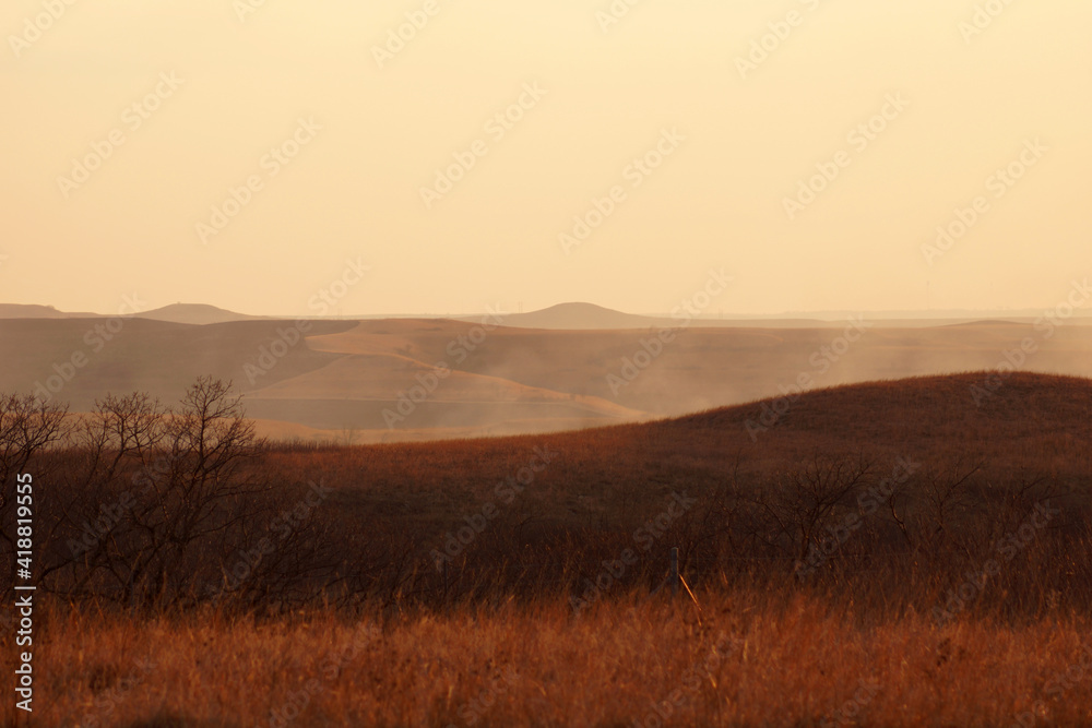 Prairie hills hazy with smoke during a wildfire on the open range. Peaks are visible in the distance.