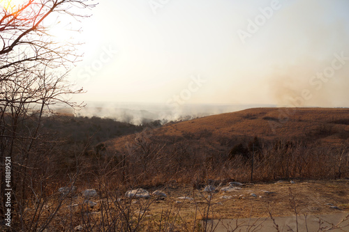 Smoke from a wild fire in the distant hills, dry grassy hillside in the foreground