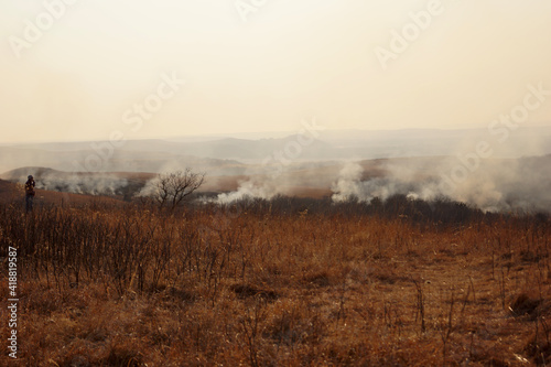 A hiker observes a wildfire in the dry, grassy hills and valley.