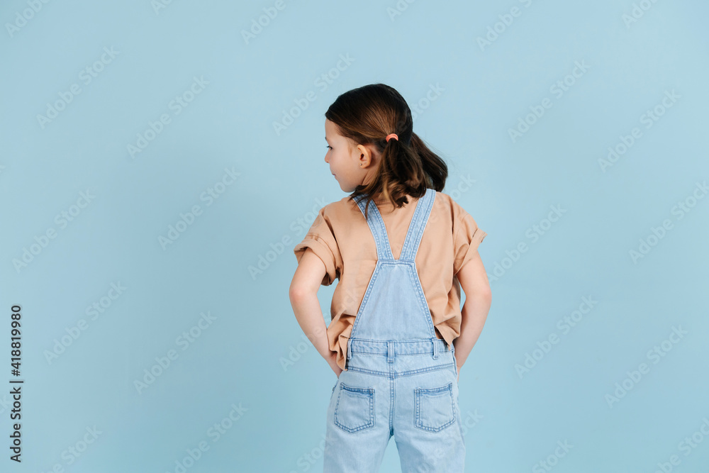 Fashionable little girl posing with her back turned over blue background. Fashionable little girl posing with her back turned over blue background.