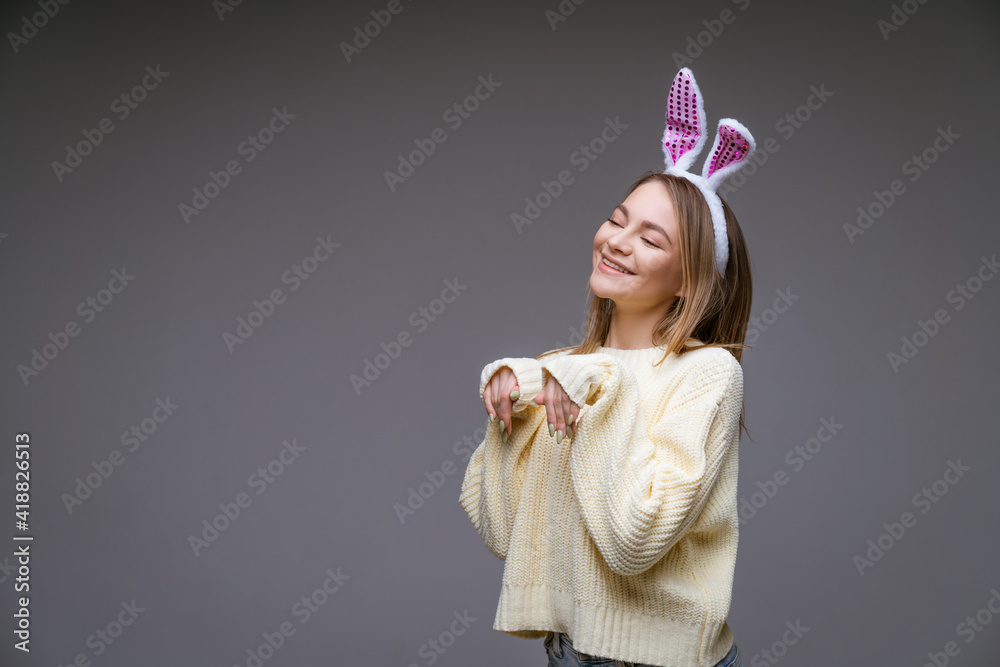 young woman, blonde, wearing white bunny ears and a light sweater on a gray background
