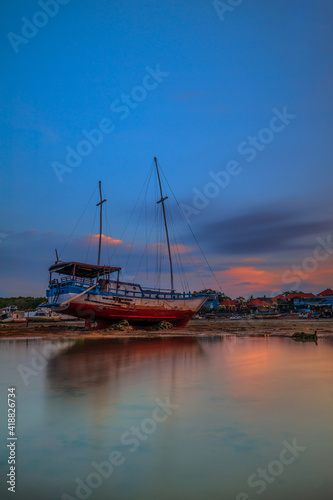 Old abandoned ship on the ocean shore. Broken ship. Sunset view. Blue sky with white motion clouds. Vertical layout. Copy space. Benoa harbor, Bali