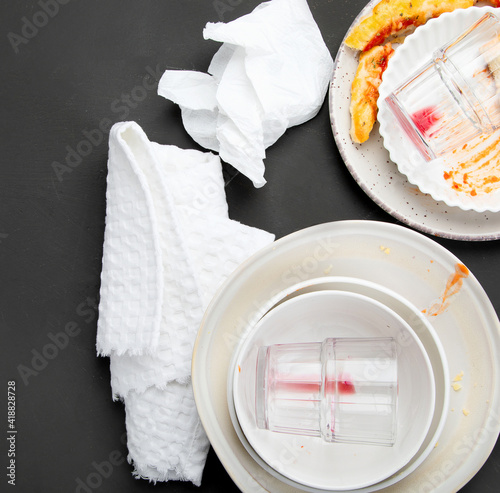 Pile of empty and dirty plates with food leftovers on dark background.