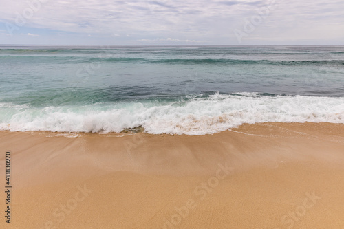 Seascape background. Sandy beach, milky foam waves, blue ocean. Scenic waterscape. Horizon line. Cloudy sky. Nature and environment concept. Daylight. Copy space. Dreamland beach, Bali