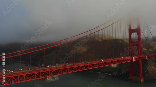 Aerial tilt down shot of vehicles on famous bridge over bay by mountains, drone flying over Golden Gate Bridge under fog - San Francisco, California