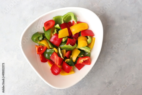 Fresh raw yellow, green, red bell peppers, and onions placed in a white bowl. Diced colorful capsicum. chopped colorful veggies for Chinese preparation. Healthy vegetable background with copy space.