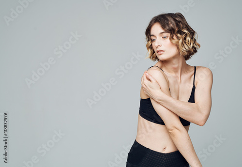 slender woman in sportswear touches herself with hands on a gray background