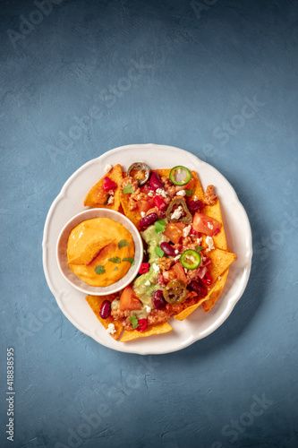 Nachos with ground beef, guacamole and cheese dip, shot from above on a blue background