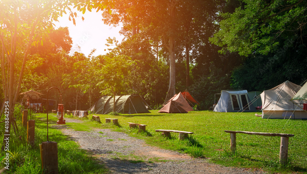 Obraz premium Morning sunlight on surface of various field tents group on green lawn in campsite area at natural parkland