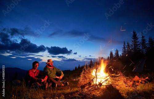 Fotografie Two hikers sitting at fire and enjoying warm evening in the mountains