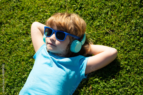 Listening to music. Summer boy in headphones. Kid in park lying on grass.