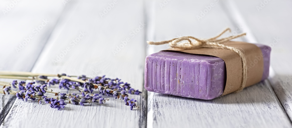 Natural handmade lavender soap with dried lavender flowers on a white wooden table, banner. Side view. Natural handmade lavender soap with dried lavender flowers on a white wooden table, banner. Side view.