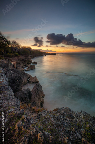 Sunset view. Seascape background. Amazing ocean view. Beach with rocks and stones. Bright sunlight on horizon line. Cloudy sky. Vertical layout. Bali.