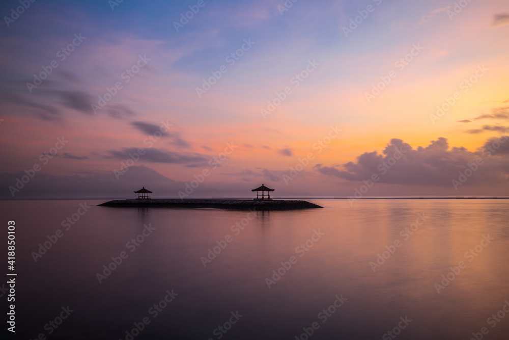 Pink sunrise. Seascape background. Traditional gazebos on an artificial island in the ocean. Water reflection. Calm water surface. Soft focus. Copy space. Sanur beach, Bali.