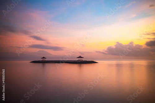 Pink sunrise. Seascape background. Traditional gazebos on an artificial island in the ocean. Water reflection. Calm water surface. Soft focus. Copy space. Sanur beach  Bali.