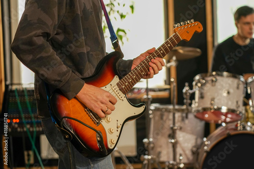 The guy plays the electric guitar to record the sound. He holds a guitar in his hands