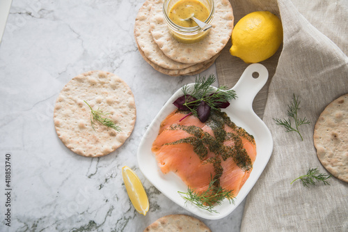 Gravlax Graved Lachs, ein roh gebeizter Fisch mit Dill auf Platte mit Hovmästarsås Senf Soße, Knäckebrot, Zitrone und Leinen Tuch auf hell Marmor Hintergrund photo