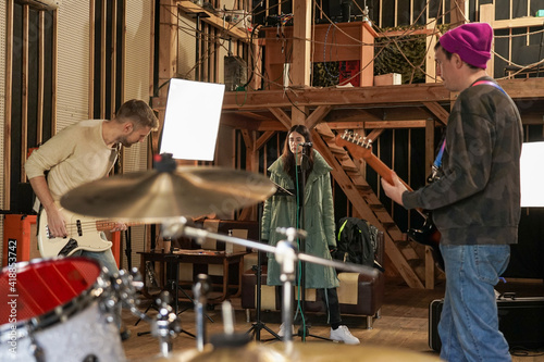 A girl sings into a microphone, two guys play an electric guitar.