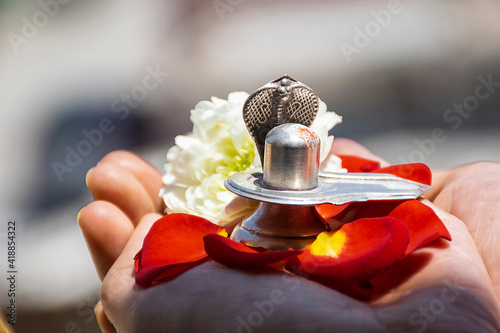 Stock photo of a man holding and worshiping silver shivlinga which is icon of lord shiva on the occasion of mahashivratri , flowers around the shivlinga in bright sunlight at Bangalore city  photo