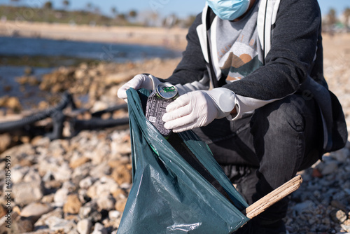 Man with mask and gloves on beach of Israel collects poisonous garbage in plastic bag. Oil spill in sea or ocean danger to marine animals and birds. Eco- system.