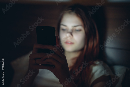 woman in the room lies in bed with a phone in her hands addiction