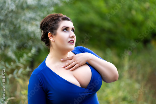Sexy plus size model in blue dress with a deep neckline outdoors, beautiful fat woman with big breasts in nature