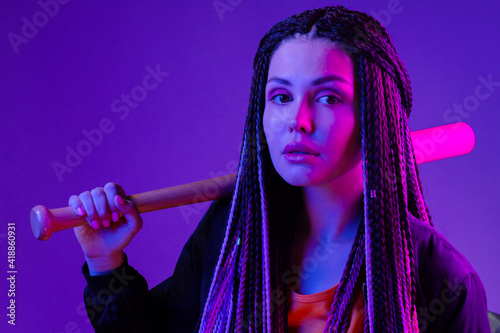 Young woman with afro braids holding a bit on a shoulder in neon lught photo