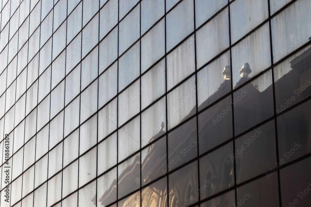 A building with an old architecture is reflected on the geometric mirrored glass of an office building with a modern architecture. Architectural concept from the urban environment A building with an old architecture is reflected on the geometric mirrored glass of an office building with a modern architecture. Architectural concept from the urban environment