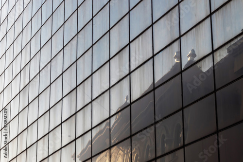 A building with an old architecture is reflected on the geometric mirrored glass of an office building with a modern architecture. Architectural concept from the urban environment