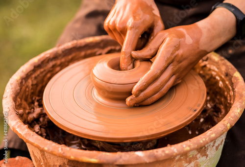 Close-up view of man working on pottery wheel and making clay pot outdoor, selective focus