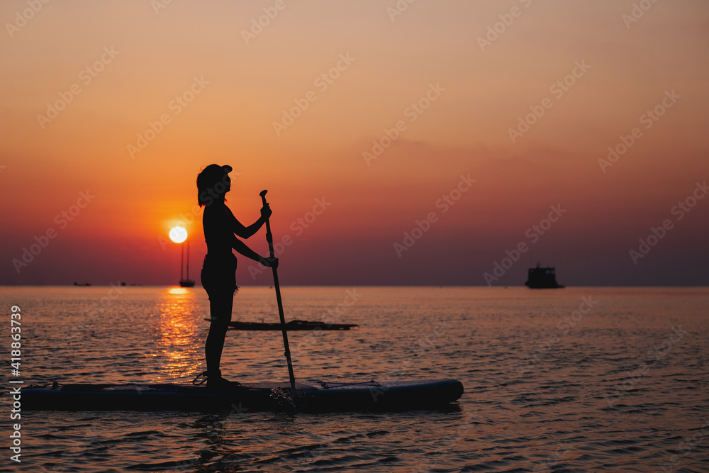 Silhouette image of a young woman on stand up paddle board in a sea before sunset