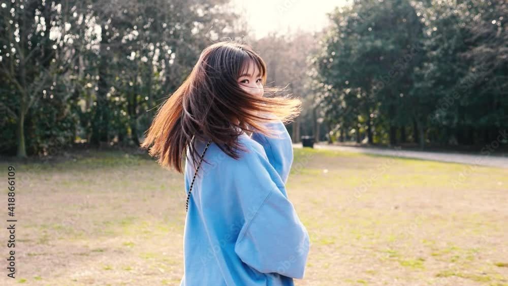 Beautiful Chinese young woman turning back with shiny black long hair and smiling with aim you gesture in forest park, slow motion footage. Beautiful Chinese young woman turning back with shiny black long hair and smiling with aim you gesture in forest park, slow motion footage.