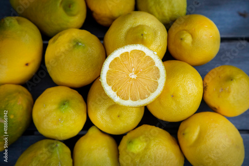Slice of lemon along with a group of lemons on a wood table