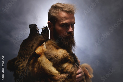 Fényképezés Low key portrait of a bearded war shaman in bearskin with an ancient ax in his hands