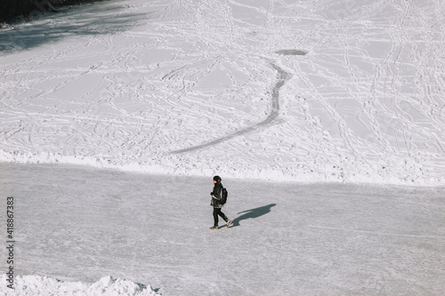 An adult man, a tourist walks through the fresh snow and slippery ice in black clothes in the winter, exploring the country. Photography, copy space.