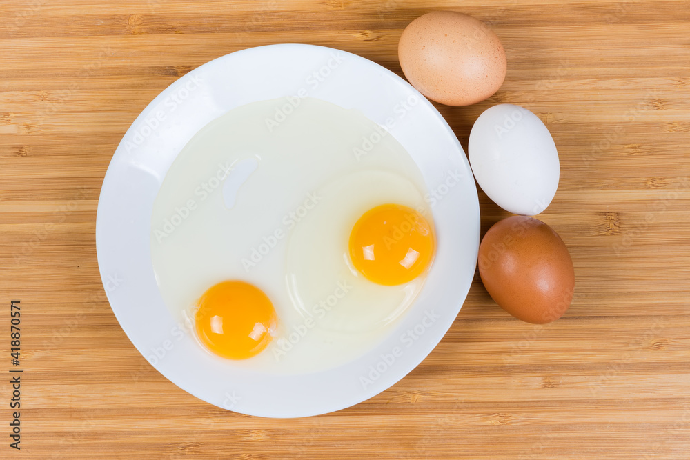 Broken eggs on dish and whole eggs beside, top view Broken eggs on dish and whole eggs beside, top view