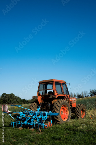 Red tractor with blue harrow on a farm.