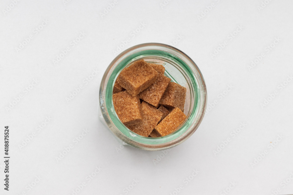 Glass cup with brown sugar cubes and cork top lid against white background seen from top. Glass cup with brown sugar cubes and cork top lid against white background seen from top.