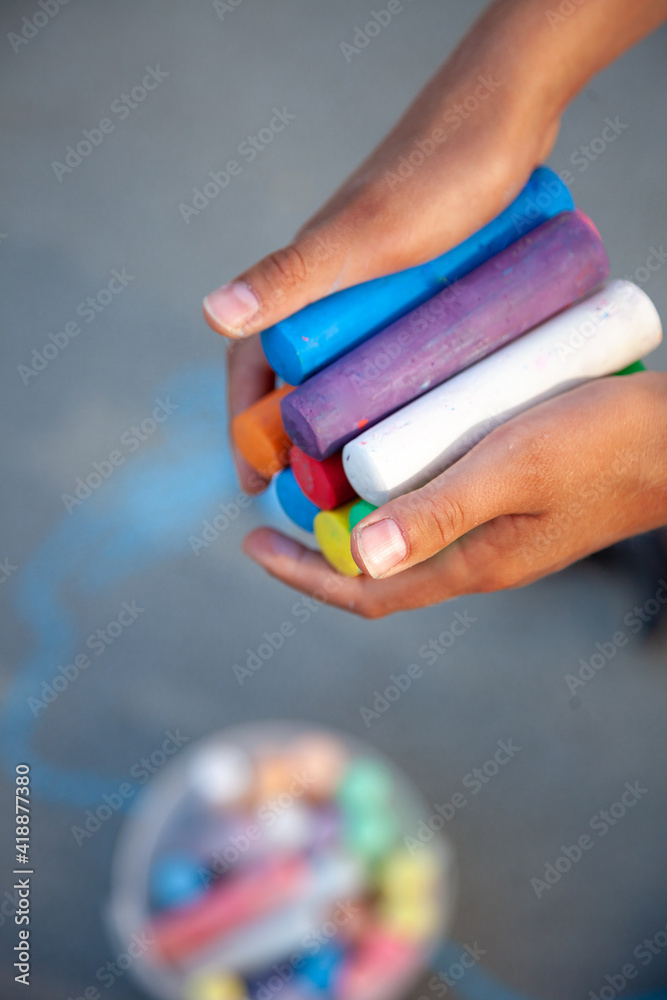 Fototapeta premium Chalks. Large multi-colored crayons in children's hands. The child holds the chalk. Draw on the street. Fascinating drawing for children