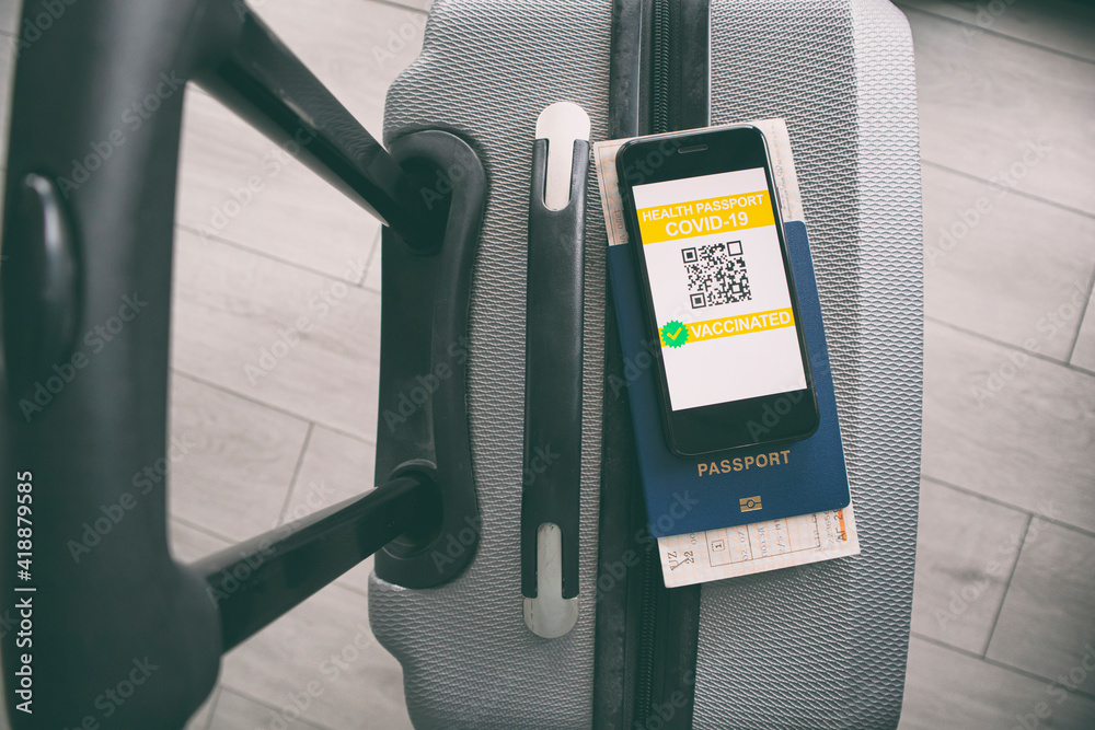 Mobile phone on the suitcase and health passport of vaccination certification on the screen